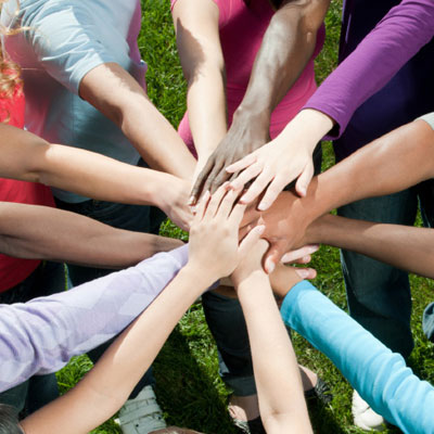 People standing in a cirlce, putting their hands in the middle on top of each other.