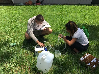Two undergraduate technicians from the University of Florida collect groundwater leachate samples below a residential lawn in Gainesville, FL. The photo shows one student measuring the volume of leachate collected and preparing to filter a sub-sample for dissolved nutrients, while the other student maintains the pump and records data. Photo by Alexander J. Reisinger.
