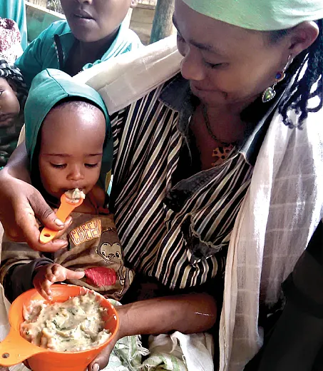 A caregiver in southern Ethiopia feeds a toddler using the Healthy Baby Toolkitâa bowl and slotted spoon that indicate how much and what texture porridge to feed young children. Photo by A. Frezer.